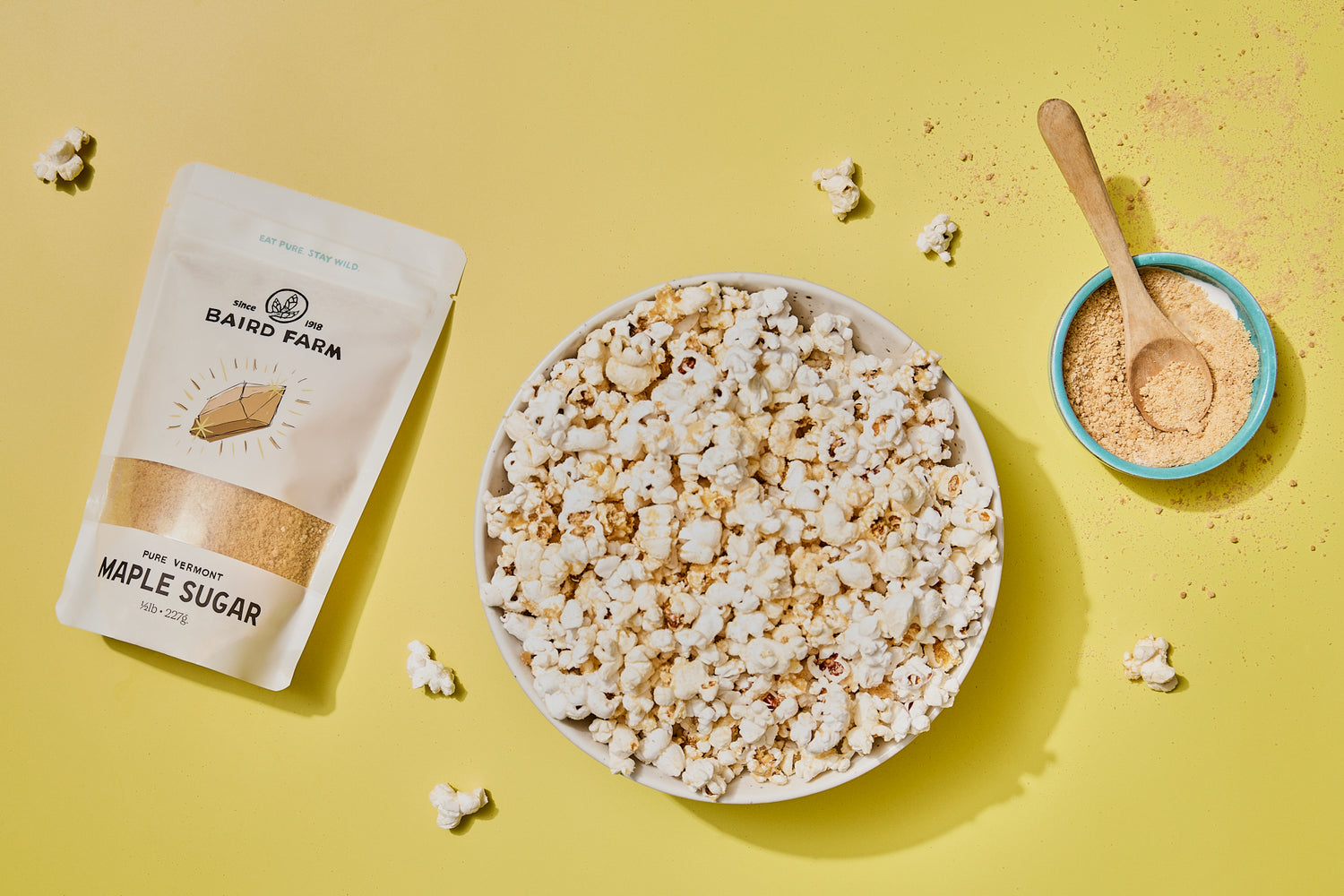 Maple sugar popcorn with a bowl of popcorn, a package of maple sugar, and a small bowl of seasoning on a yellow background.